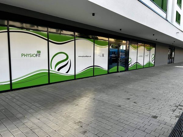 Die Fensterfront eines Physiofit-Studios zeigt ein modernes grünes Design mit Wellenmuster auf einem Gehweg.