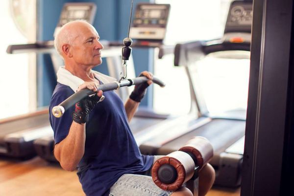 Ein älterer Mann trainiert konzentriert an einem Fitnessgerät im Rahmen der Krankengymnastik.